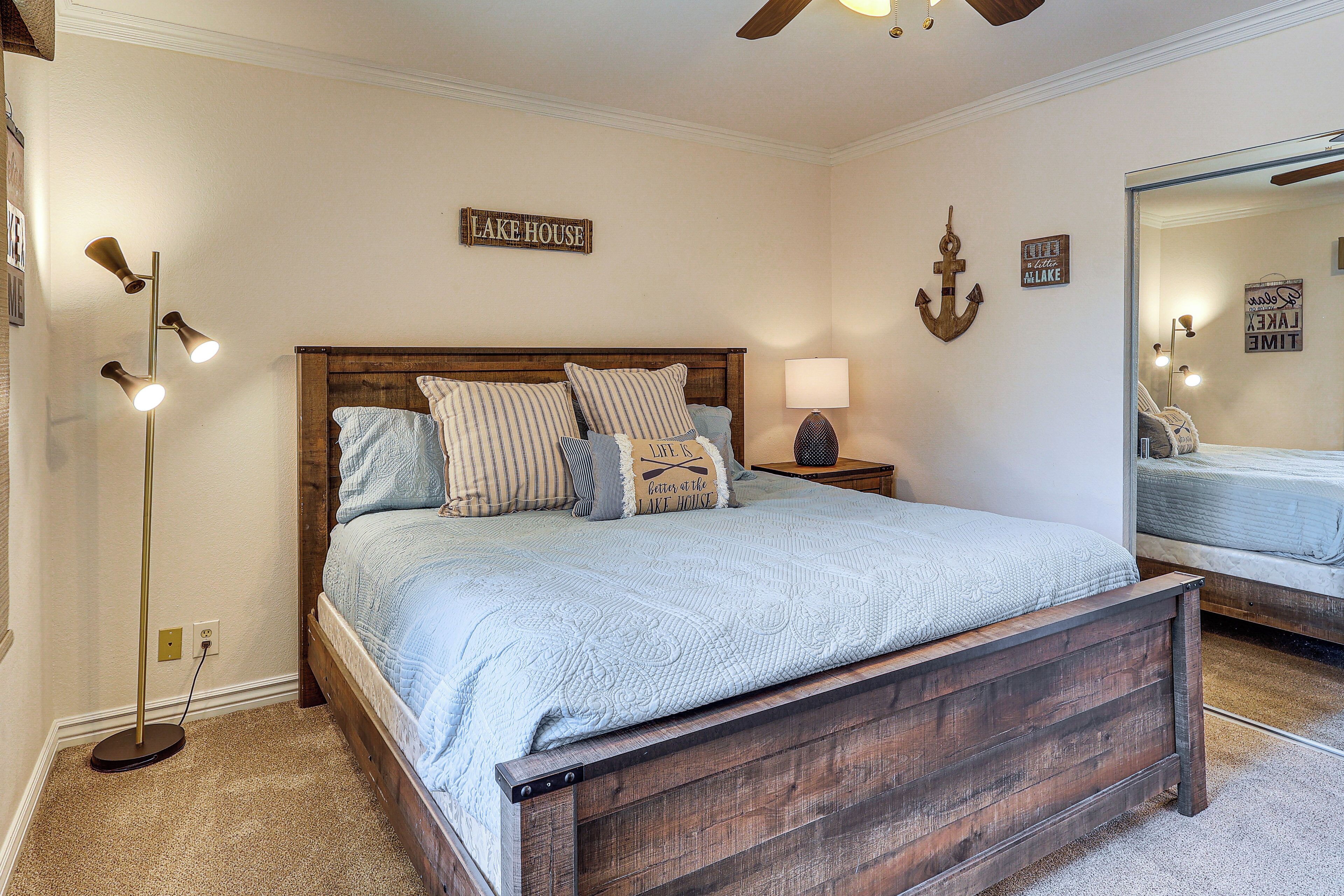 Une chambre à coucher avec un lit en bois, une lampe de chevet et des décorations murales, dont un panneau indiquant « MAISON AU BORD DU LAC ».