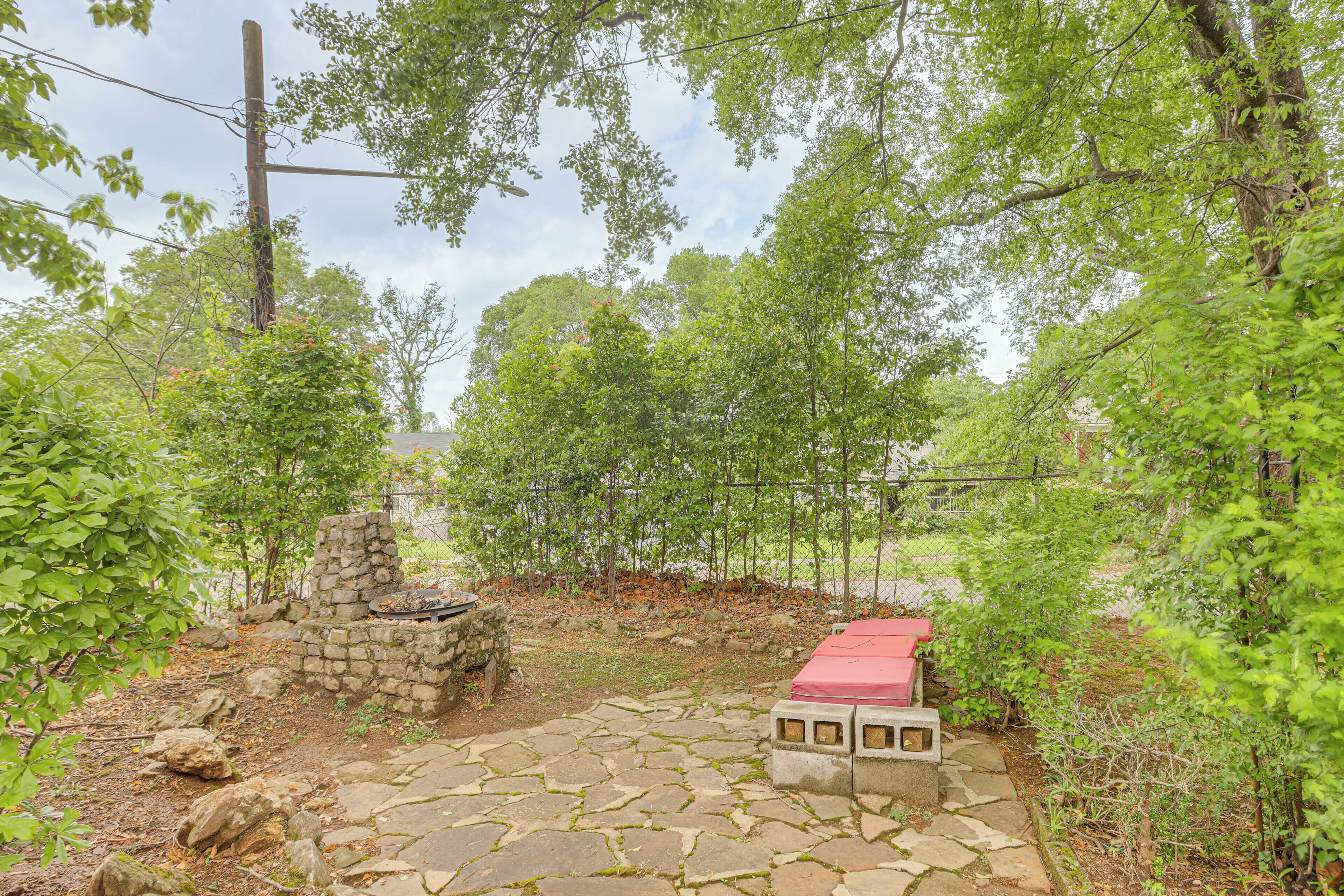 Un patio de piedra con un banco rojo, rodeado de follaje y un muro de piedra.