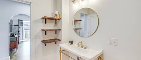 Ein Badezimmer mit einem weißen Waschbecken, goldenen Armaturen und Holzregalen.