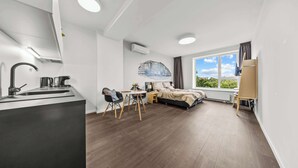 Een moderne kamer met een keukenhoek, een bed, een bureau en een groot raam.