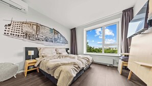 Een moderne hotelkamer met een groot bed, een flatscreen televisie, een raam met uitzicht op groen en een muurschildering.