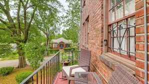 A brick building with a balcony, wicker furniture, and a view of a tree and another building in the background.