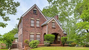 A brick house with a front porch, a garage, and a well-maintained lawn.