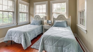 A bedroom with two beds, a nightstand, a lamp, and large windows.