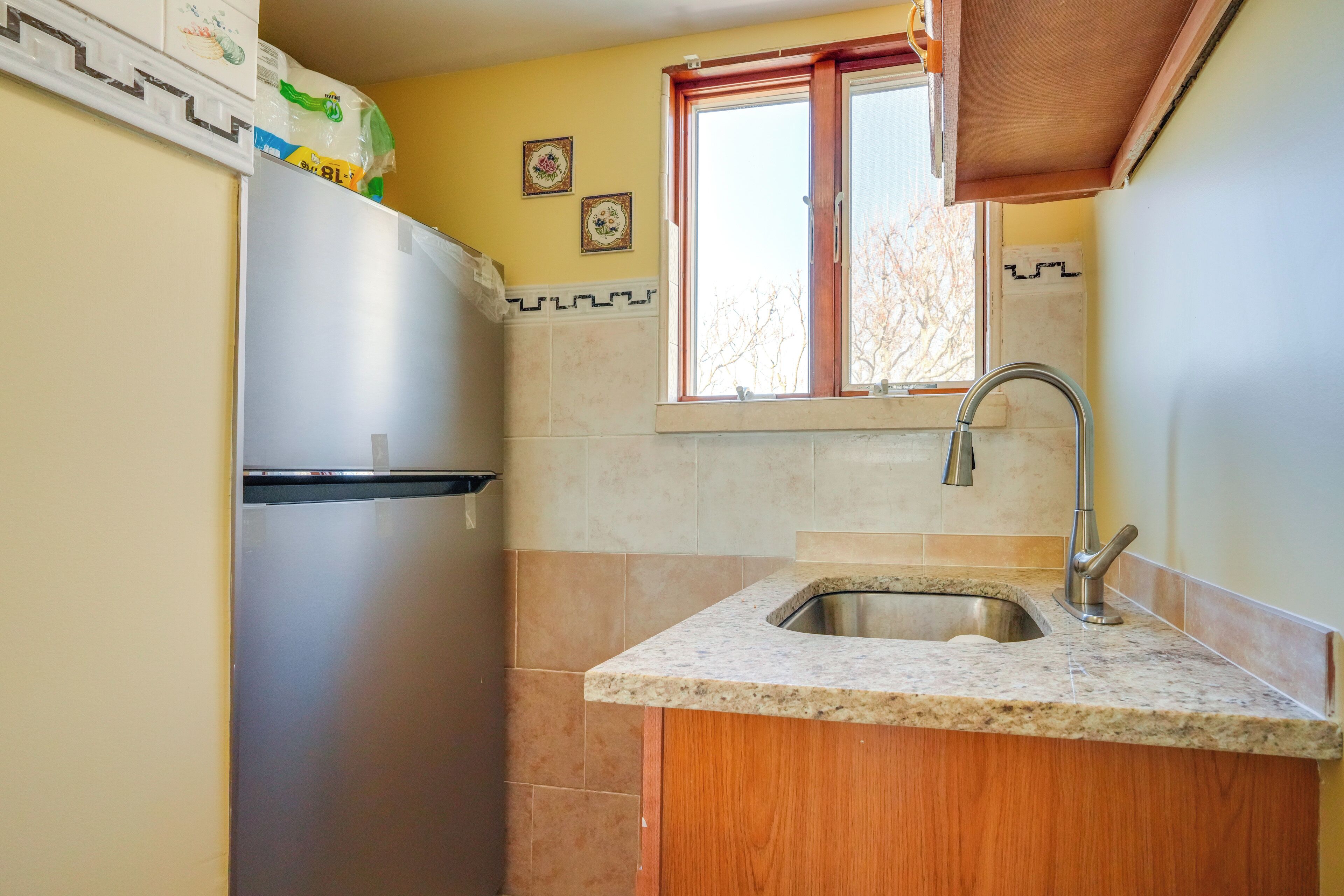 A compact kitchen with a stainless steel refrigerator, a sink with a modern faucet, and a window above the sink.