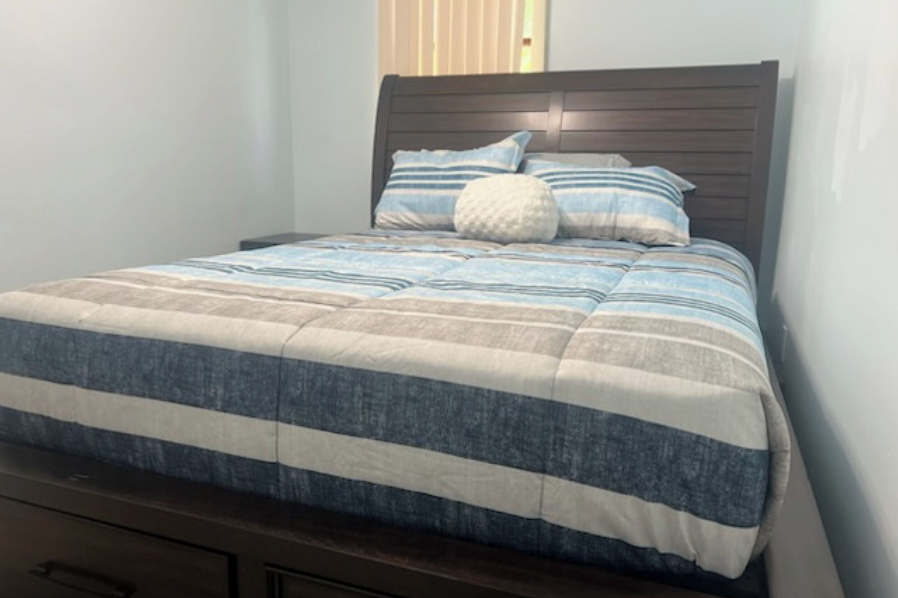 A bed with a striped bedspread, a wooden headboard, and two pillows.
