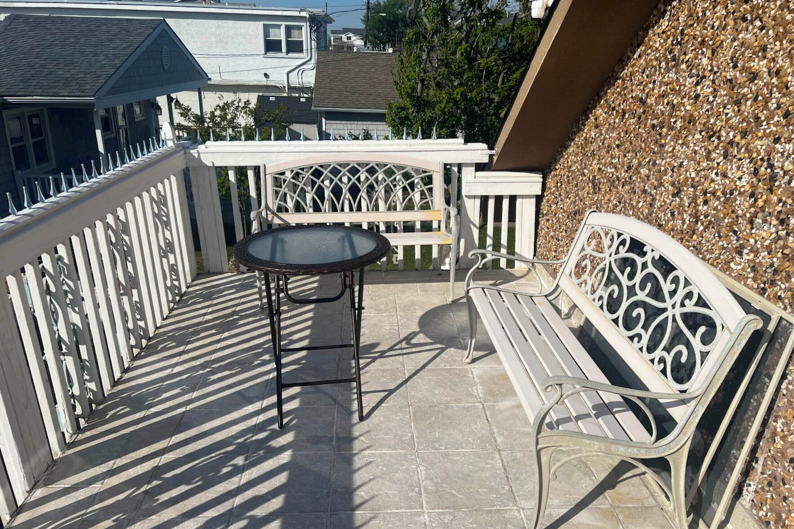 Un balcon avec une table ronde et un banc, entouré d’une clôture blanche en bois.
