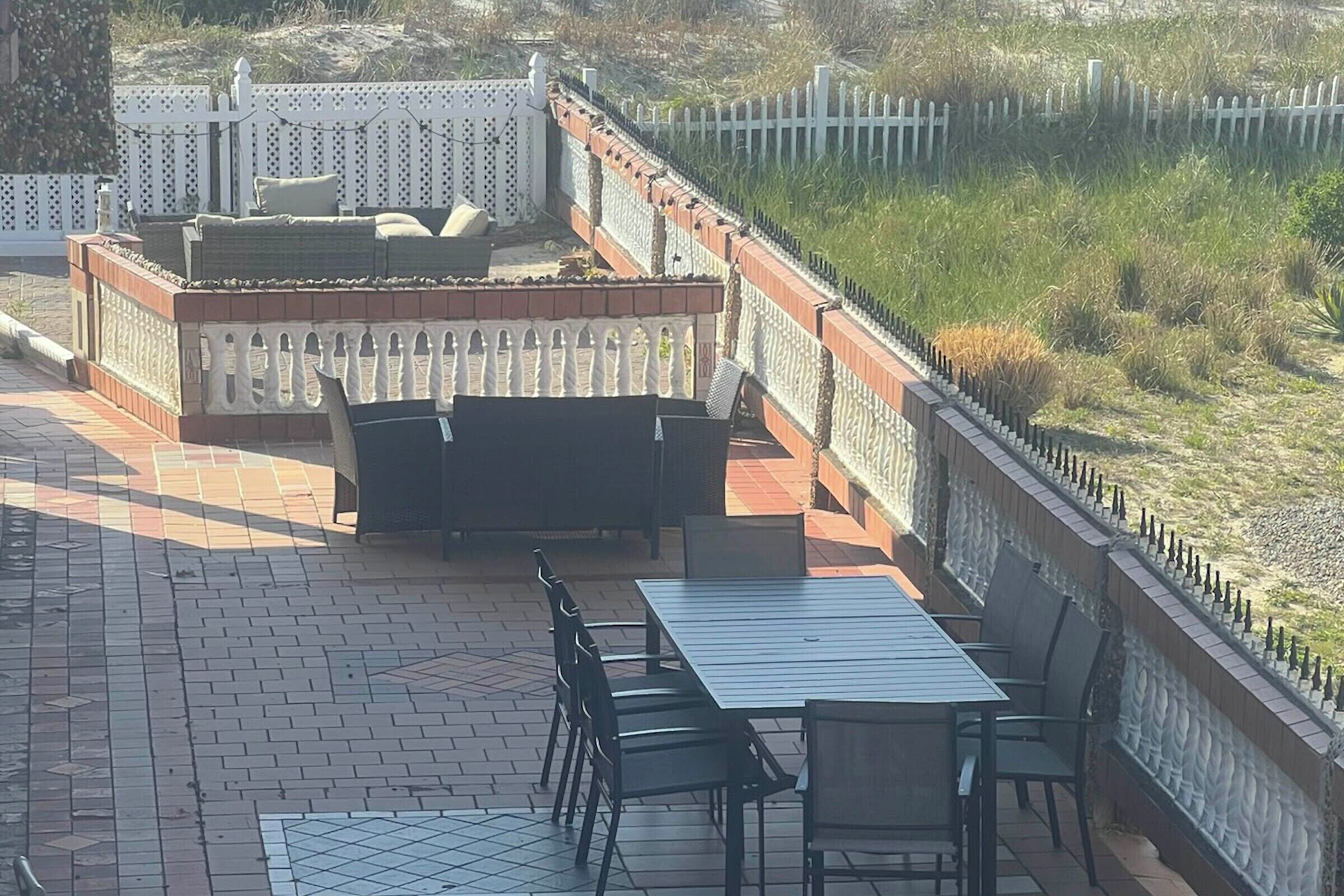 Eine Außenpatio mit Tisch und Stühlen, einer Sitzgruppe mit Polstern und einem weißen Zierzaun.