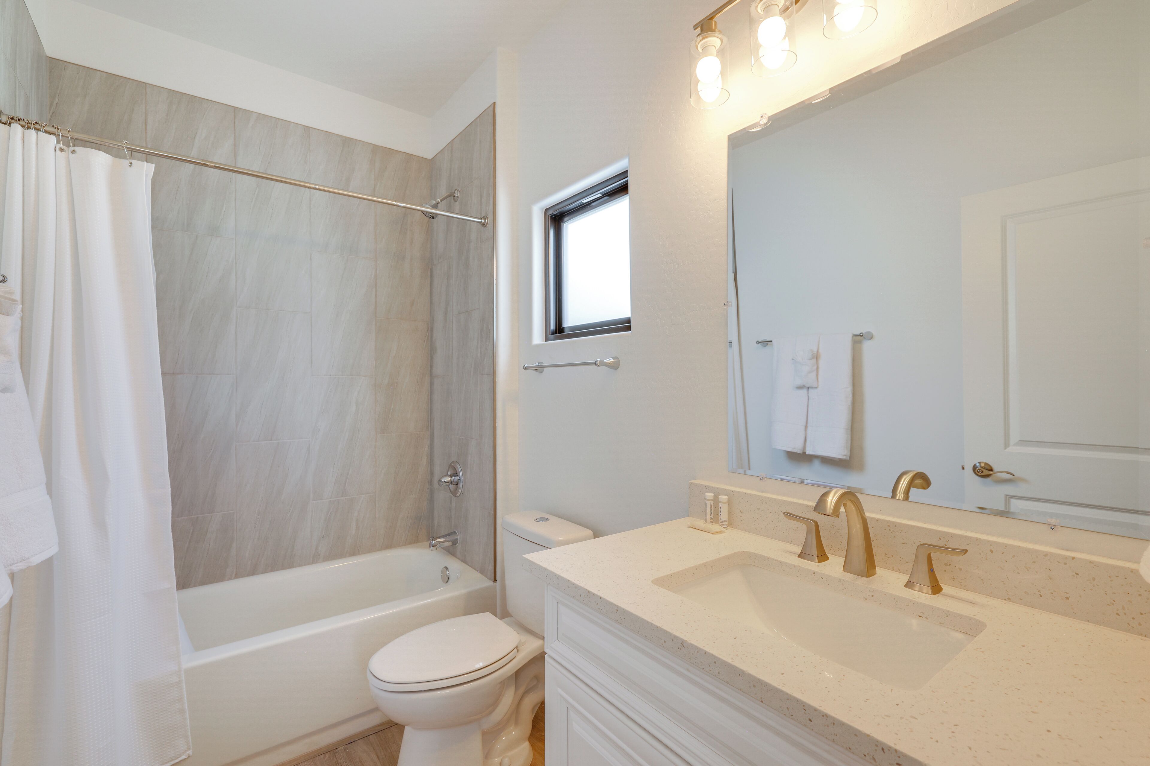 A modern bathroom with a bathtub, toilet, and vanity with a sink and mirror.