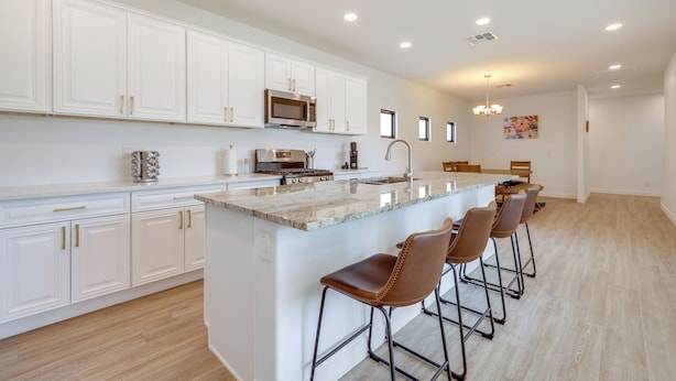 A modern kitchen with white cabinets, a granite countertop, and a central island with bar stools. - PHX Group Retreat By Dtwn! New Build w/ Patio (Phoenix)
