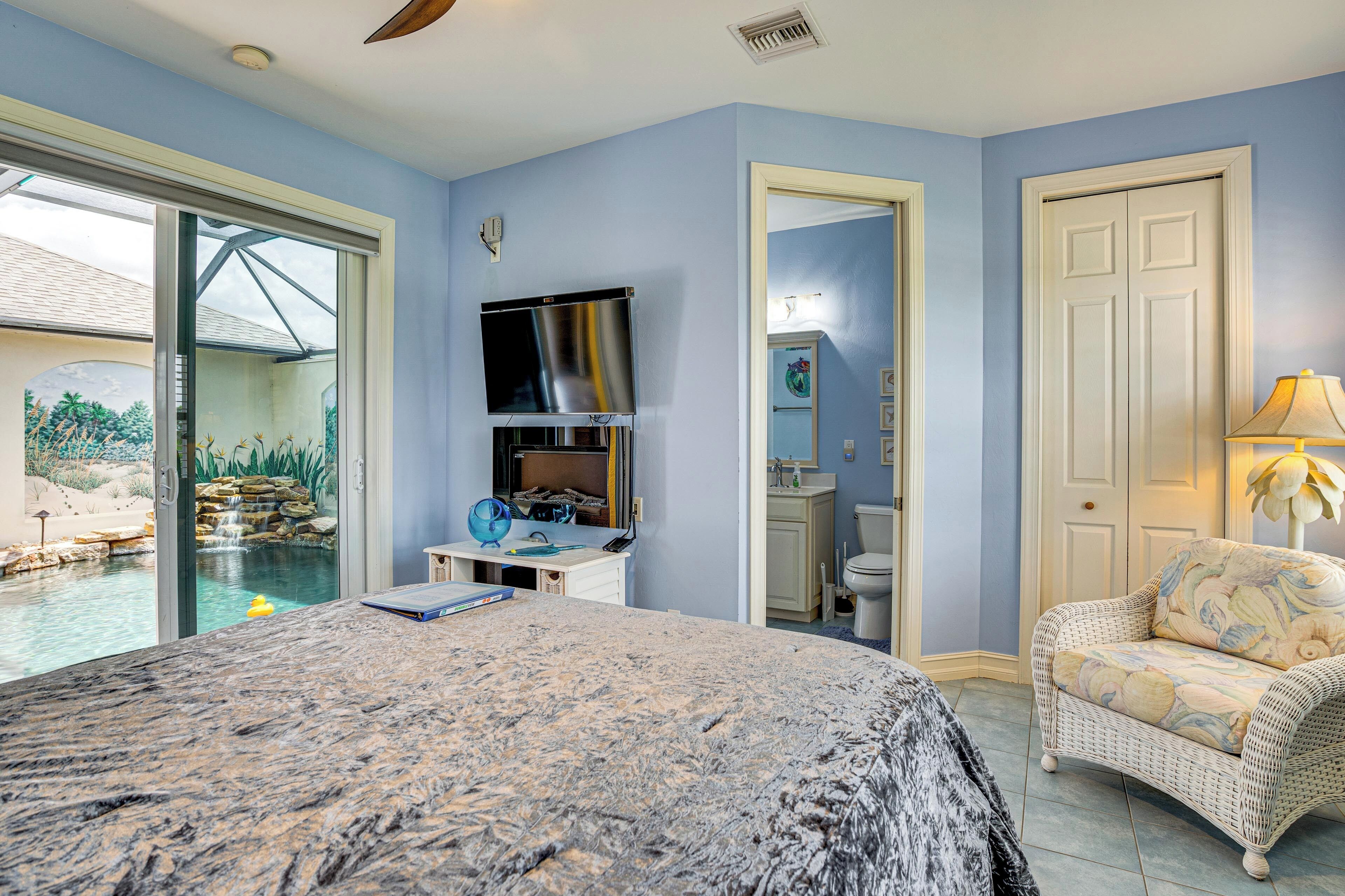 A bedroom with a large bed, a TV, a view of a pool, and a bathroom.