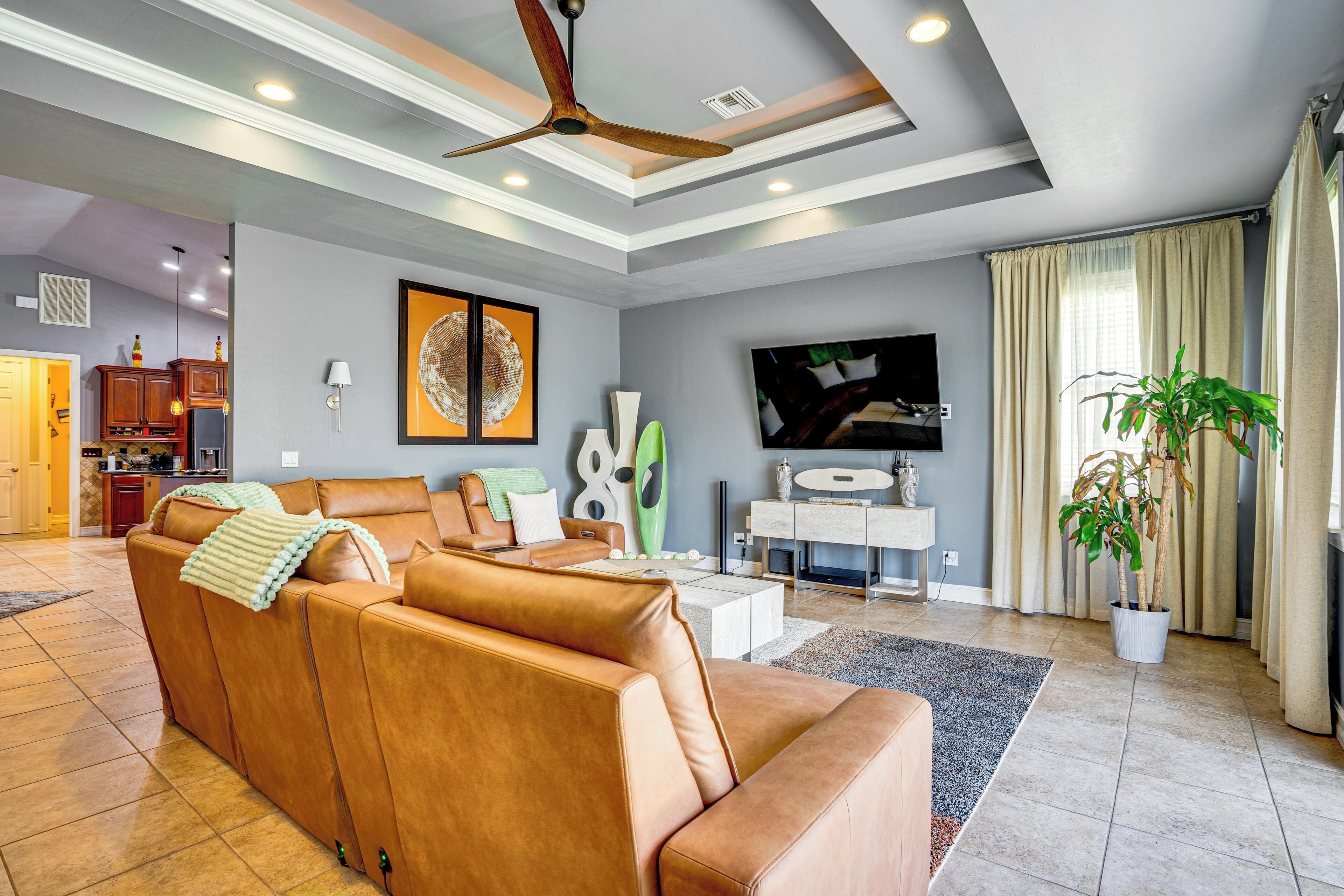 A living room with a sofa, a television, a ceiling fan, and a potted plant.