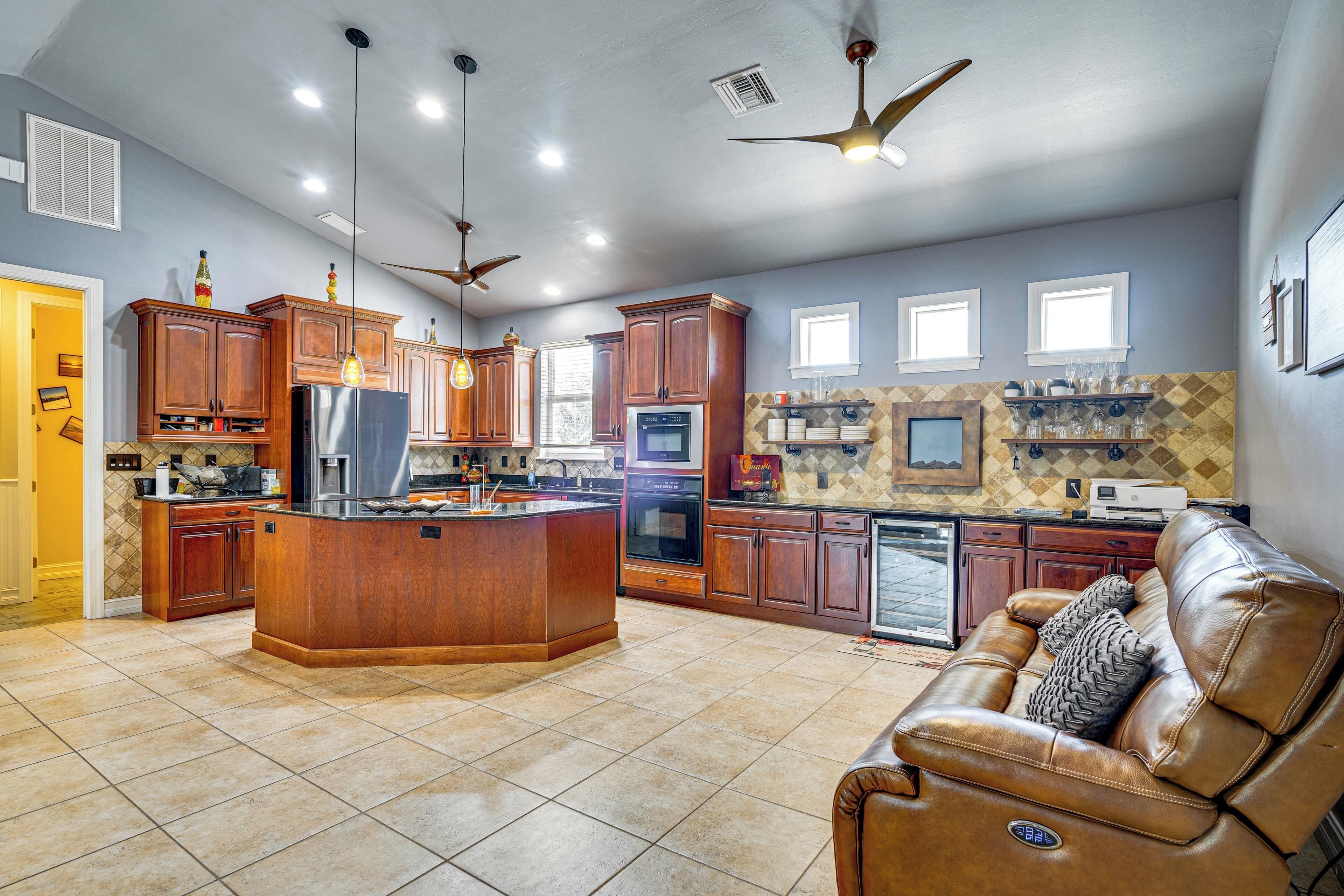 A spacious kitchen with wooden cabinets, a central island, and a leather sofa.