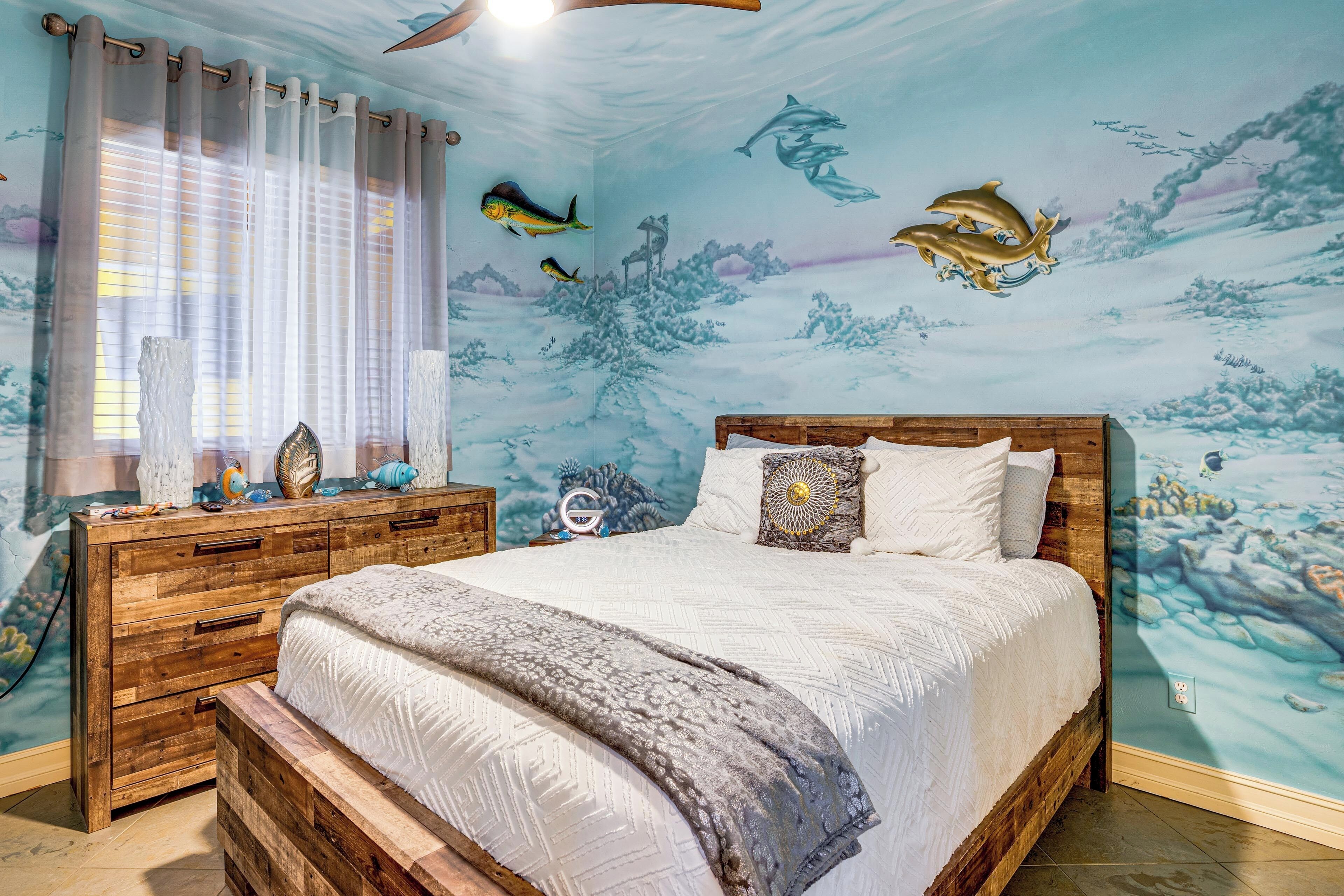 Un dormitorio con cama, cabecera de madera y un mural de peces y paisaje submarino en la pared.