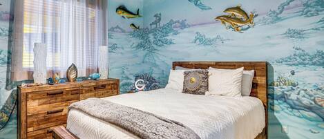 Un dormitorio con cama, cabecera de madera y un mural de peces y paisaje submarino en la pared.