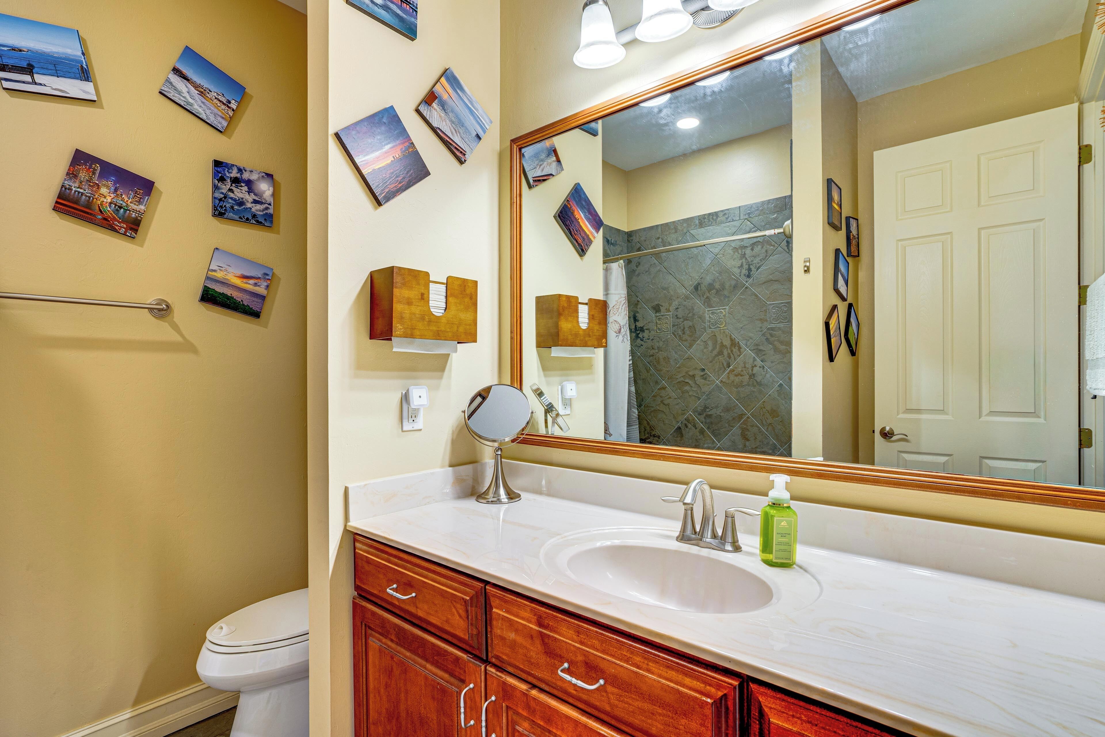 Une salle de bain avec un lavabo blanc, des meubles en bois, un grand miroir et plusieurs tableaux encadrés accrochés au mur.