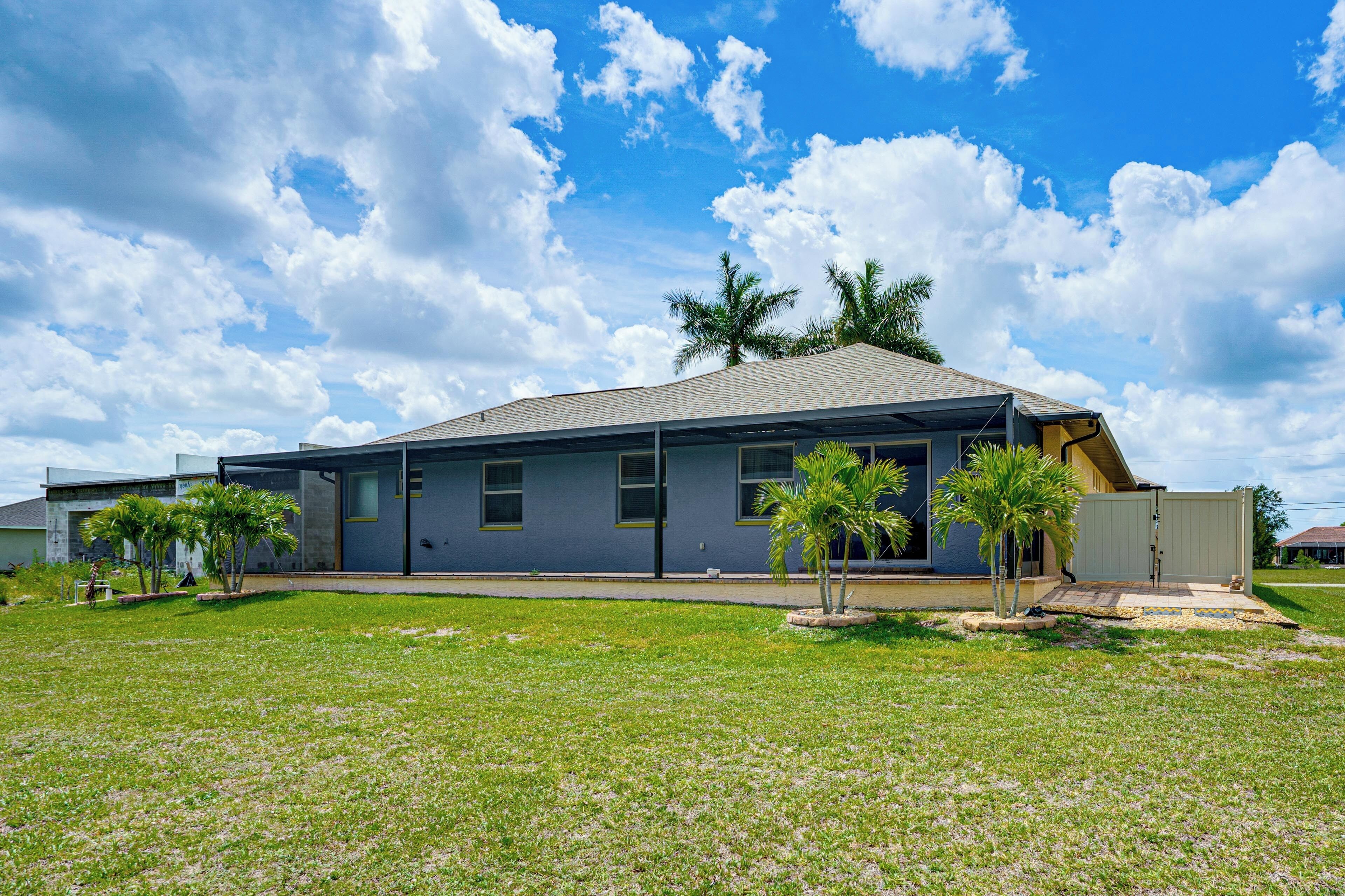 A single-story building with a flat roof, a covered porch, and a small lawn area with palm trees.