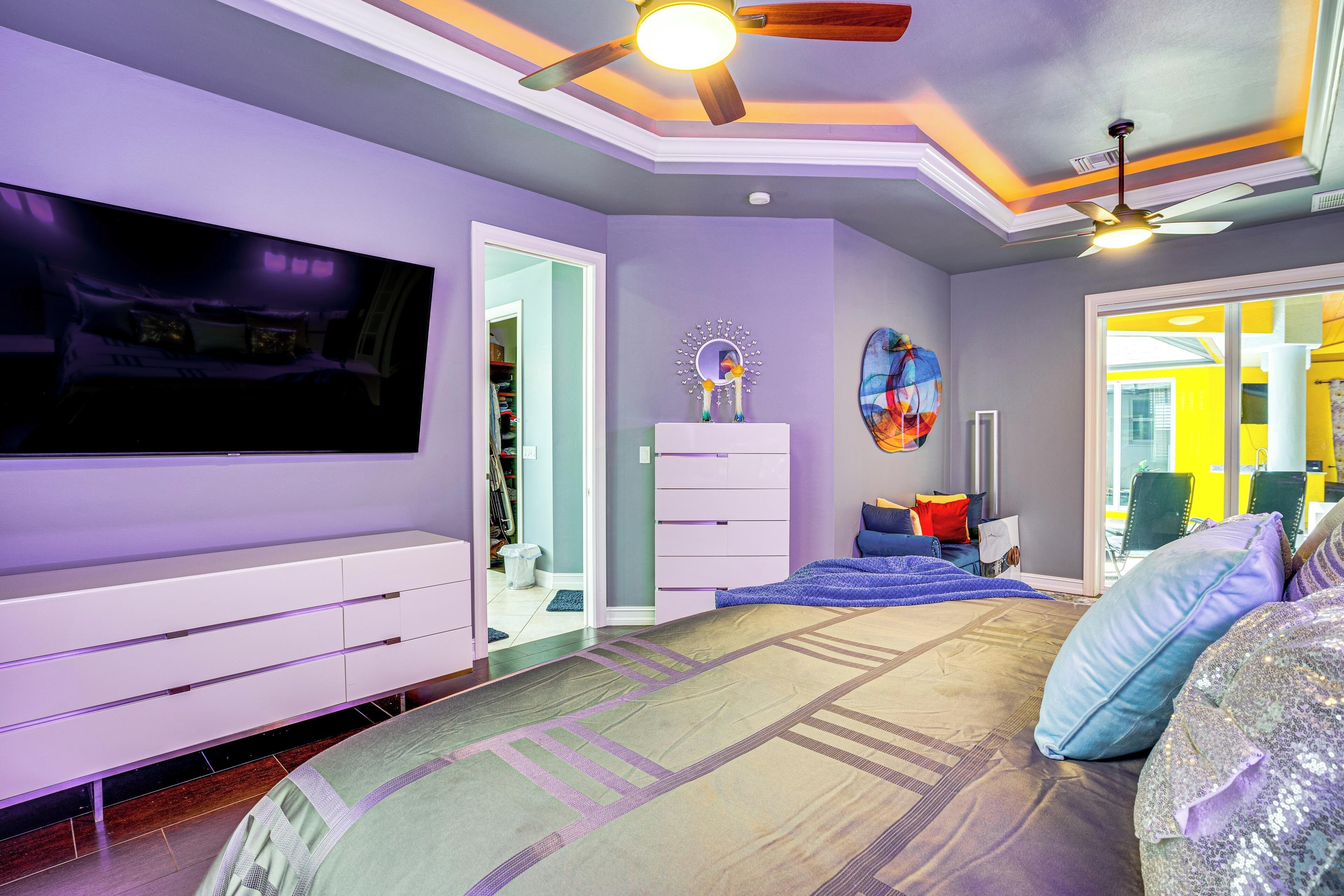 Un dormitorio con una cama grande, un ventilador de techo, un televisor montado en la pared y un aparador.