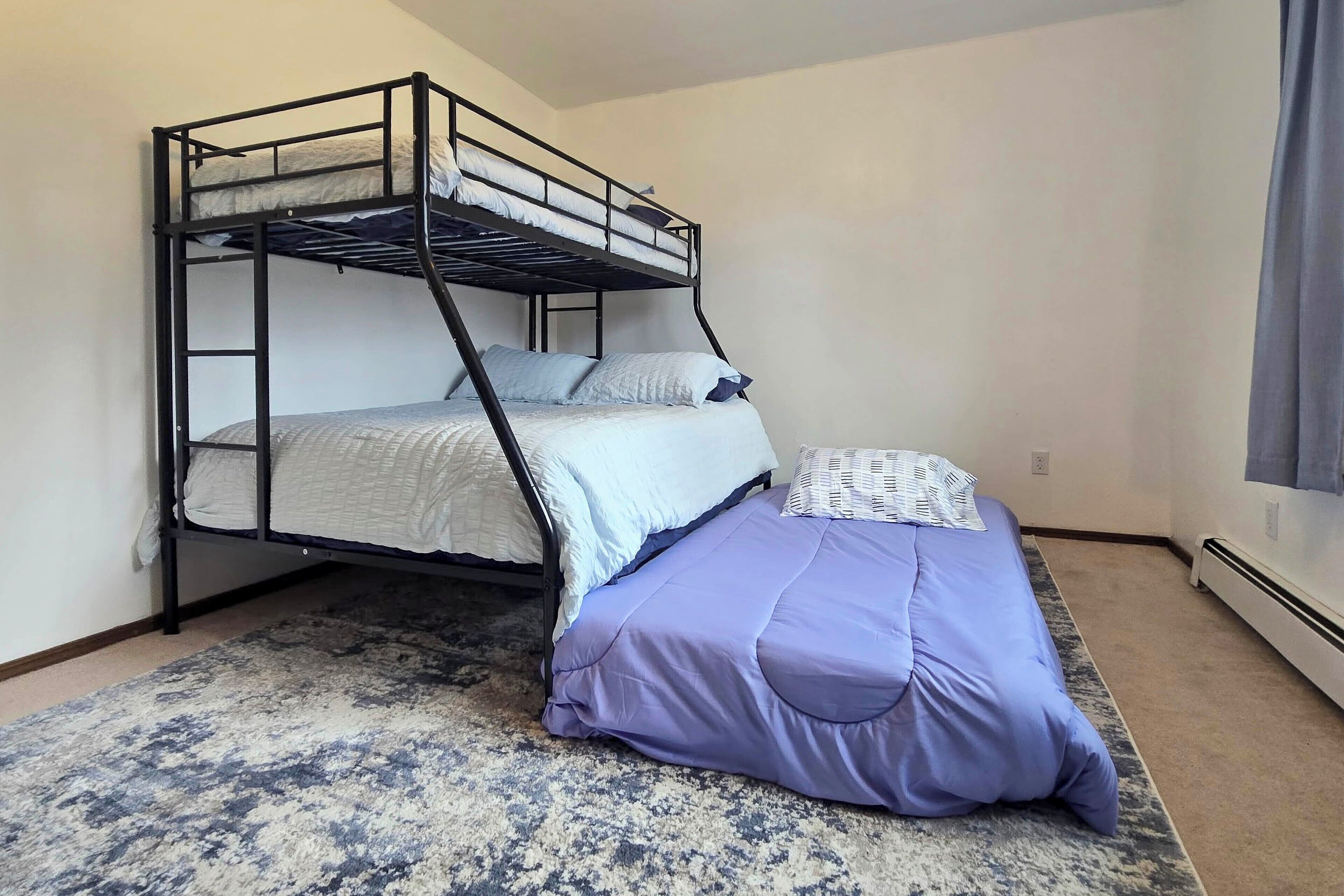 Una cama litera con una cama inferior, un colchón, almohadas, una manta azul y una alfombra estampada.