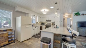 Moderni keittiö, jossa on valkoiset kaapit, suuri keittiösaareke ja riippuvalaisimet.