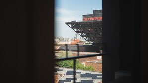 Une vue à travers une fenêtre ornée d’une grille métallique, montrant un bâtiment avec une enseigne rouge, un toit et quelques éléments de végétation.