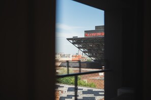 Blick durch ein Fenster mit einem Metallgitter, der ein Gebäude mit einer roten Beschilderung, ein Dach und etwas Grün zeigt.