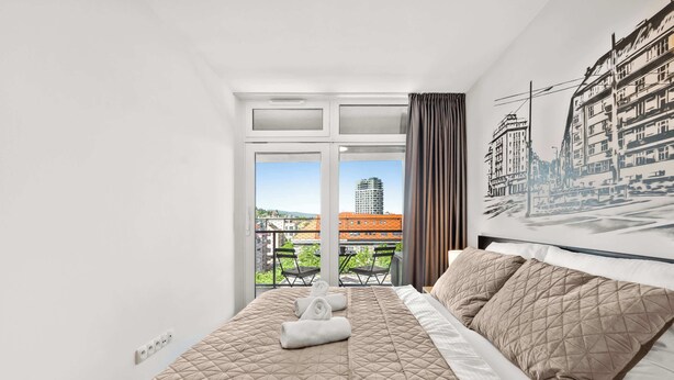 Une chambre d’hôtel avec un lit, une fenêtre avec des rideaux, un balcon avec des chaises et une vue sur la ville.