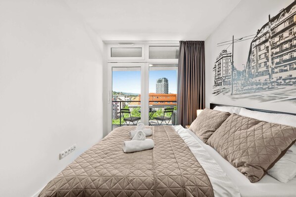 Ein Hotelzimmer mit Bett, einem Vorhangfenster, einem Balkon mit Sitzgelegenheiten und Blick auf die Stadt.