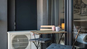 Un petit espace extérieur aménagé avec une table et des chaises, un banc et une fenêtre donnant sur des bâtiments.