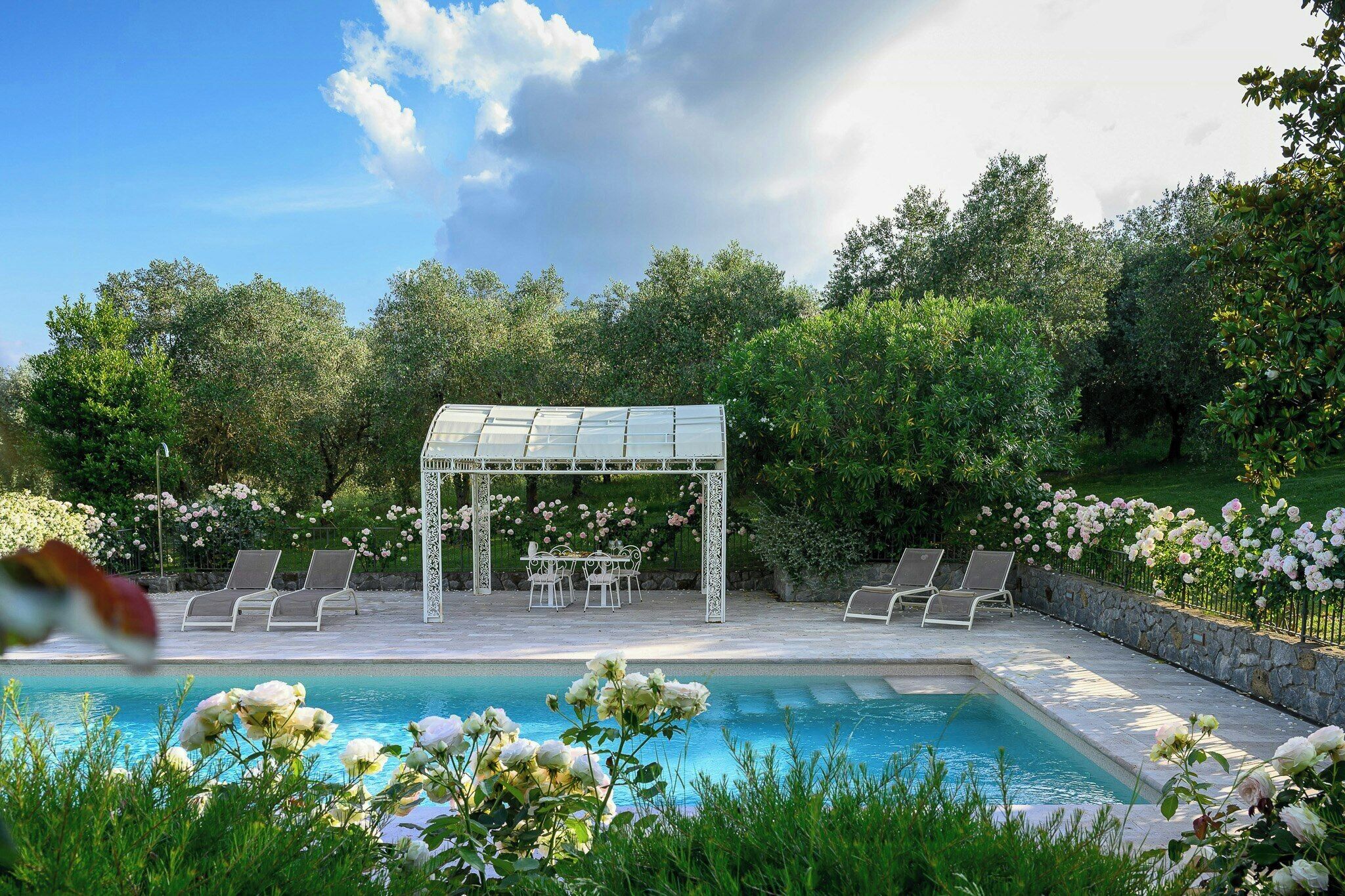 Een zwembadgedeelte met een pergola, lounge fauteuils en een rozen tuin.