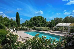Ein Schwimmbecken mit Liegestühlen und einer Pergola, umgeben von üppiger Bepflanzung und blühenden Pflanzen.