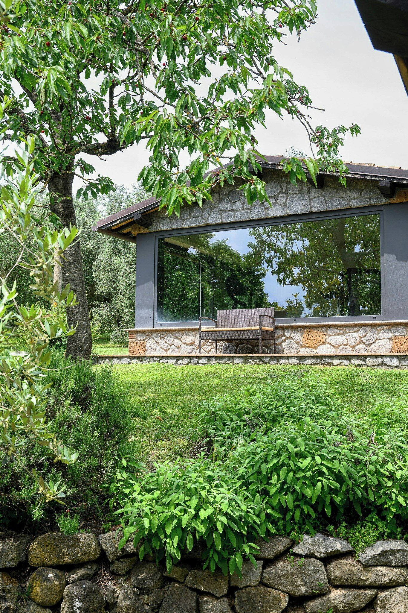 A modern house with a stone wall, a large window, and a patio with a chair.
