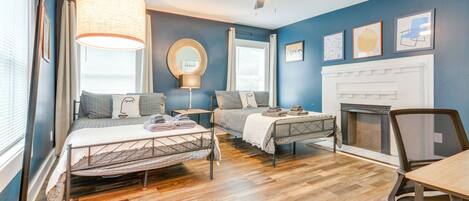 A bedroom with two beds, a ceiling fan, a fireplace, and a dining table.