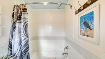 A bathroom with a bathtub, a shower curtain, a potted plant, and a framed painting on the wall.
