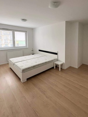 Ein Schlafzimmer mit Bett, Nachttisch, kleinem Tisch, Fenster und Heizkörper.