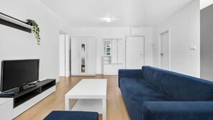 Un salon moderne avec un téléviseur à écran plat, une table basse blanche, un canapé bleu et une petite plante.
