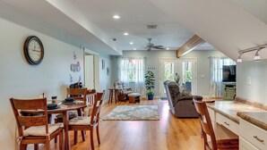 A spacious living area with a dining table, chairs, a sofa, and a kitchen area. - Fire Pit & Forest Views: Lakes Region Retreat (Holderness)