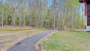 A paved path leading to a wooden cabin with a signboard. - Fire Pit & Forest Views: Lakes Region Retreat (Holderness)
