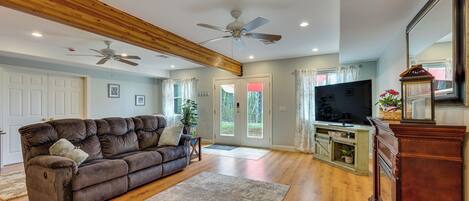 A living room with a brown sofa, wooden beams, ceiling fans, a TV, and a wooden cabinet.