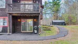 A wooden cabin with a balcony, a covered outdoor grill, and a paved driveway. - Fire Pit & Forest Views: Lakes Region Retreat (Holderness)