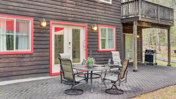 A wooden house with a balcony, a round table with chairs, and a barbecue grill. - Fire Pit & Forest Views: Lakes Region Retreat (Holderness)