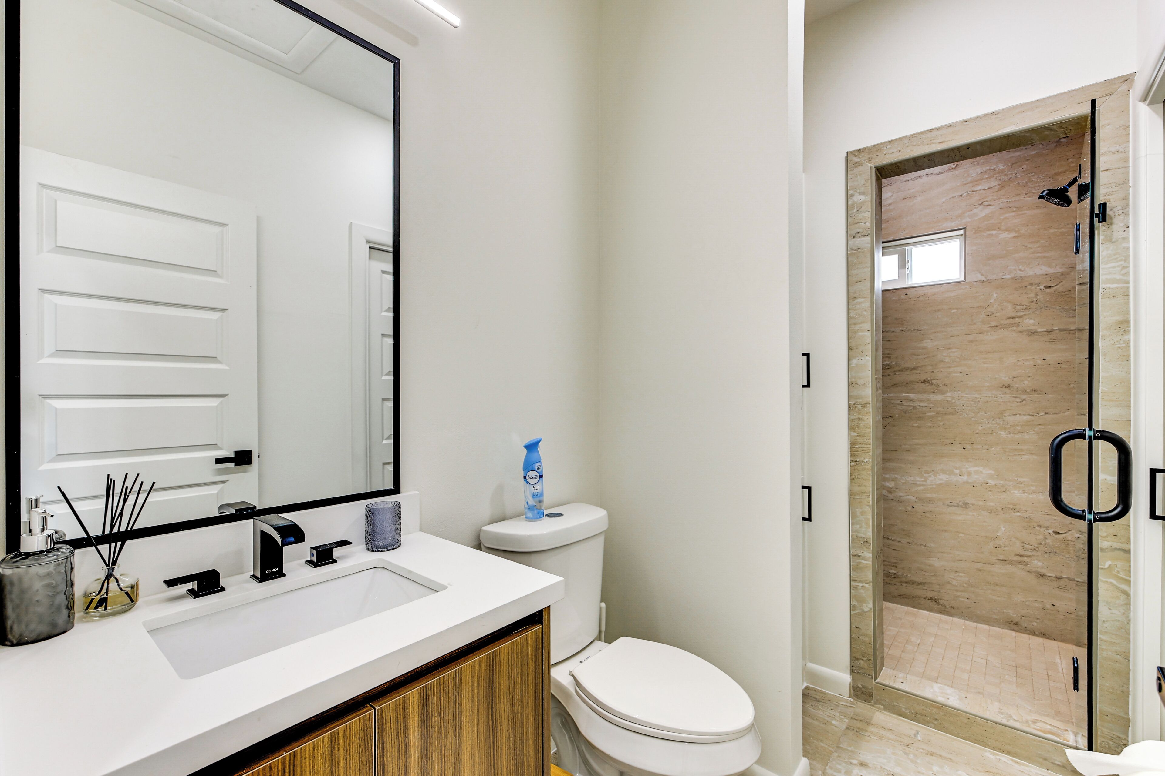A bathroom with a white sink, a toilet, a mirror, and a shower enclosure.