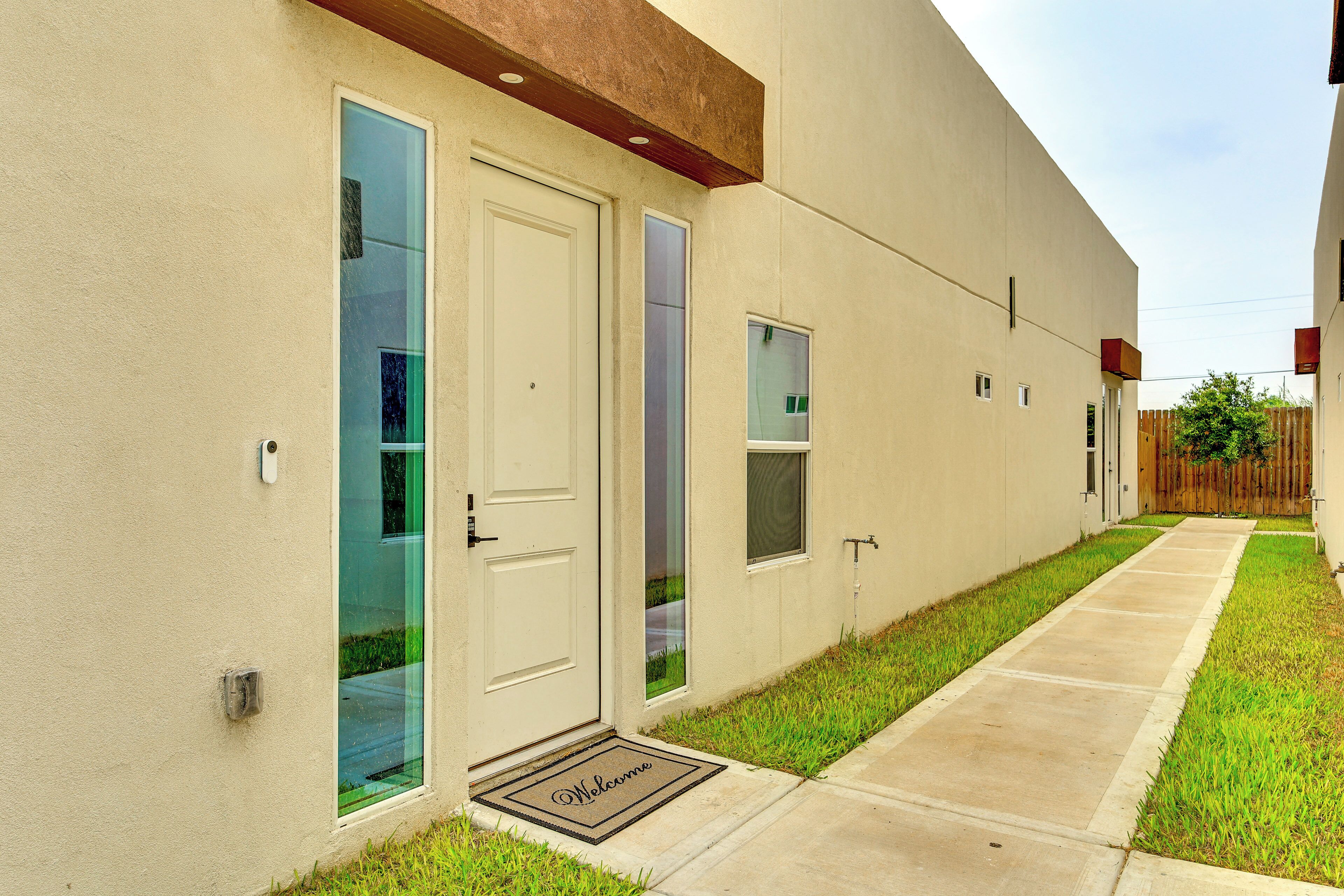A modern building with a clean facade, a welcome mat at the entrance, and a narrow pathway leading to the door.