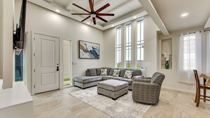 A spacious living room with a sectional sofa, ottoman, and a ceiling fan. - Modern Getaway w/ Private Patio & Grill in Mcallen (McAllen)