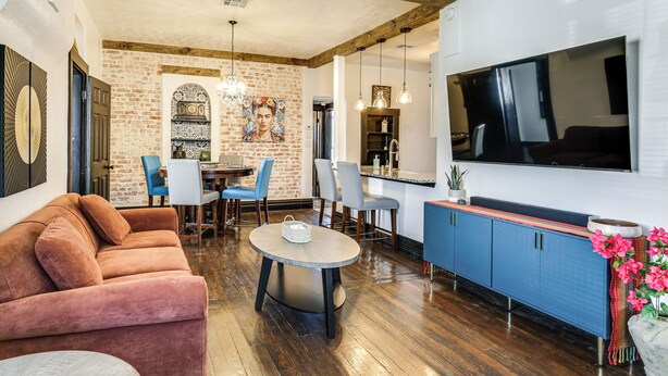 Una sala de estar con sofá, sillas, una mesa de comedor, un área de cocina y un televisor.