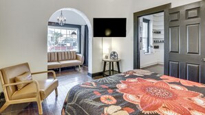 Una habitación con una cama, una silla, un televisor, una lámpara y una puerta.