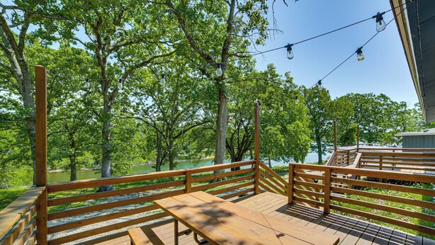 A wooden deck with benches and a railing overlooking a body of water, surrounded by trees. - Boat & Fish! Lakefront Kimberling Cove Resort Unit (Kimberling City)