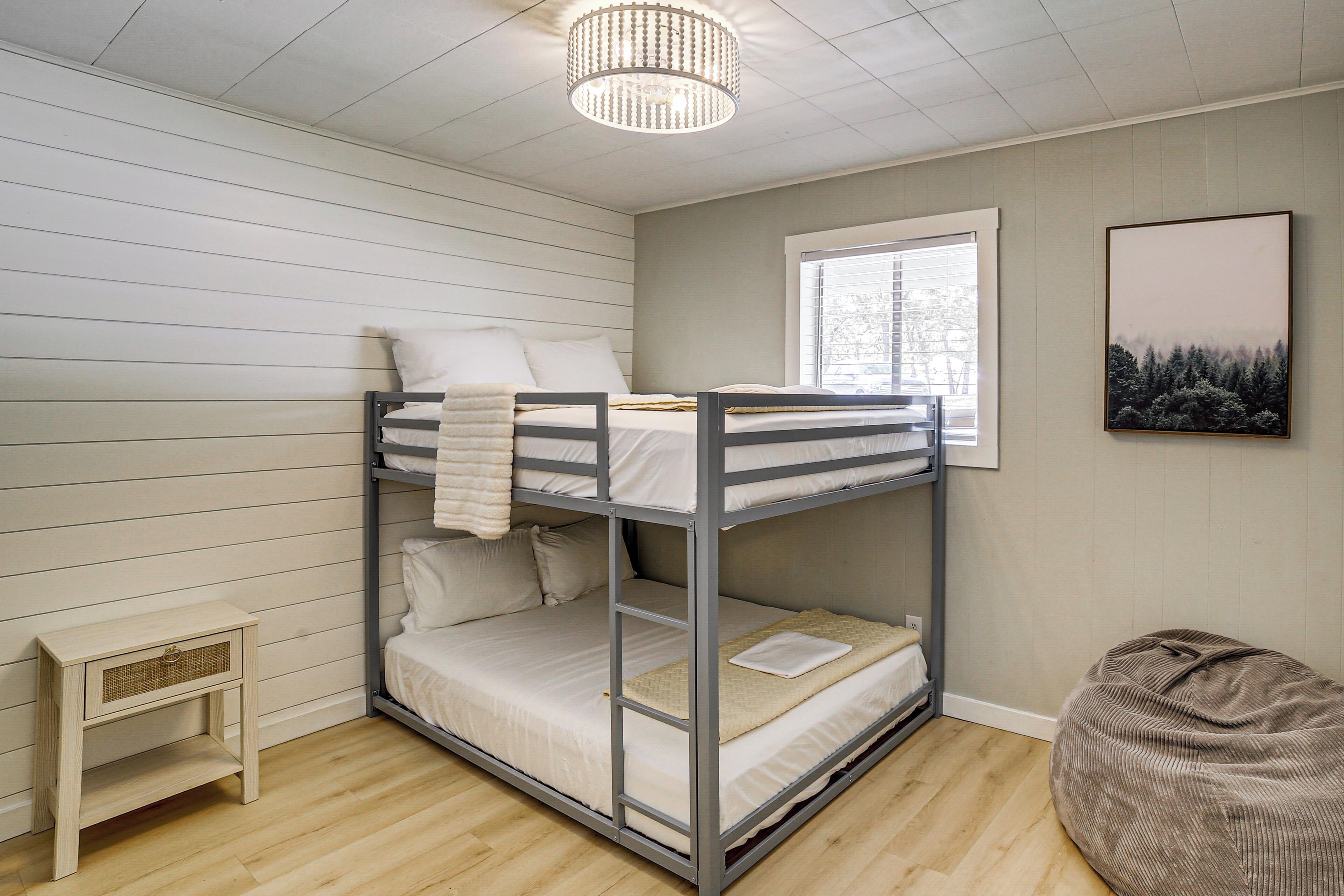 Une chambre avec un lit superposé, une petite table de chevet, un fauteuil poire et une fenêtre avec des stores.