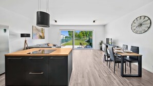 Una cocina moderna con una isla central, una zona de comedor con una mesa y sillas, y un ventanal que ofrece vistas al exterior.