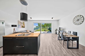 Une cuisine moderne dotée d’un îlot central, d’un coin repas avec une table et des chaises, et d’une grande fenêtre offrant une vue sur l’extérieur.